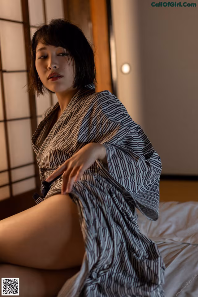 A woman in a black and white kimono sitting on a bed.