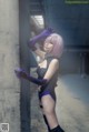 A woman in a black and purple outfit leaning against a wall.