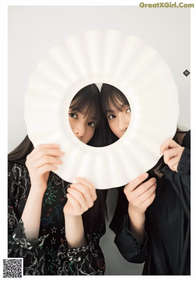 Two young women holding up a white paper fan.