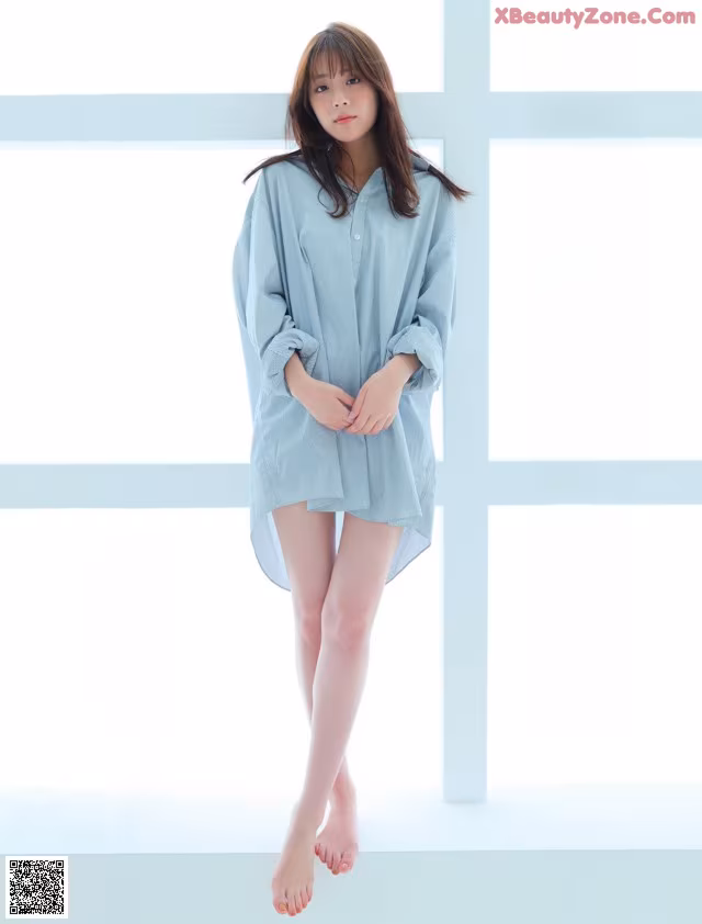 A woman in a blue shirt is standing in front of a window.