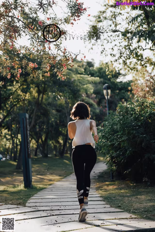 A woman jogging down a sidewalk in a park.