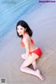 A woman in a red bikini sitting on the beach.