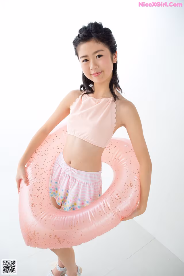A young girl in a pink bikini holding a pink inflatable ring.