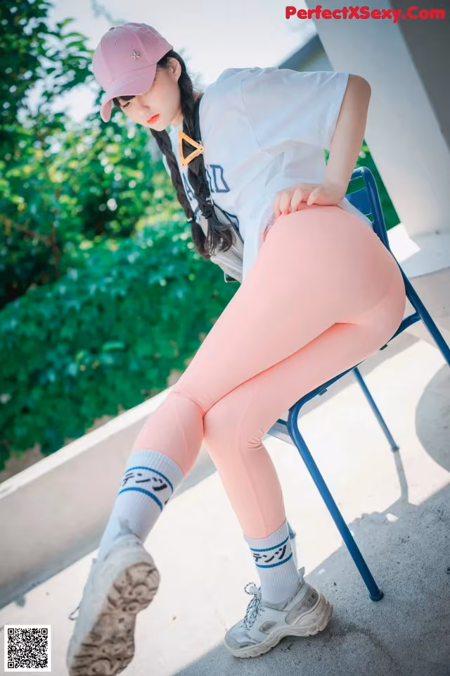 A woman sitting on a chair wearing pink leggings and a baseball cap.