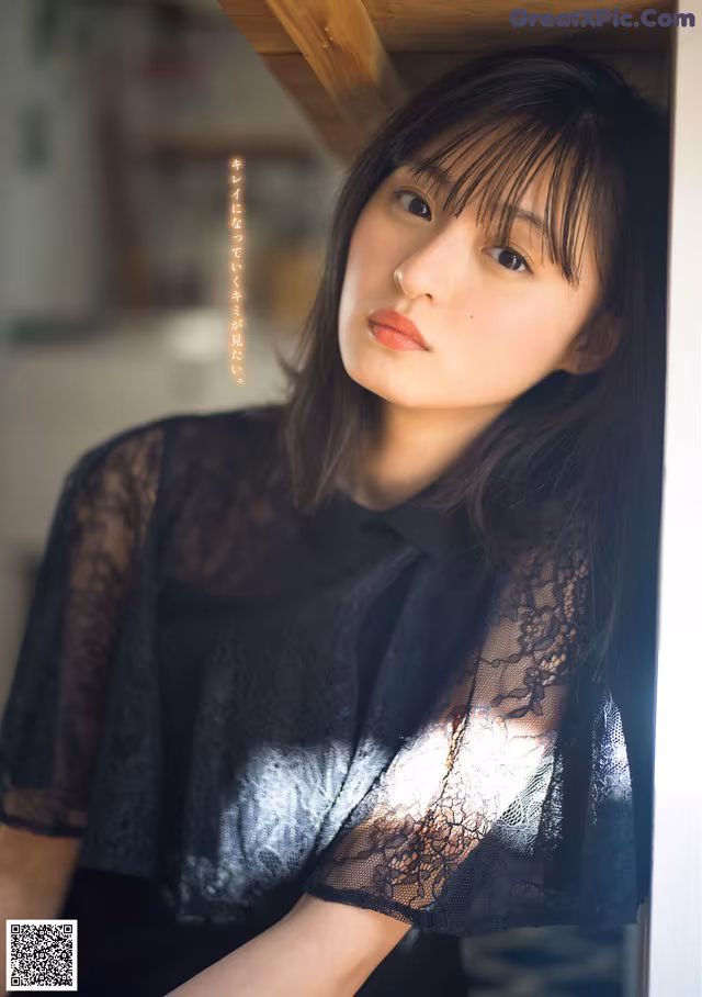 A woman in a black dress leaning against a wall.