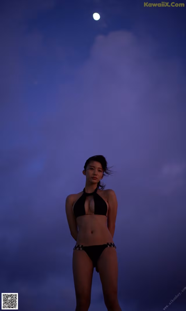 A woman in a black bikini standing in front of a full moon.