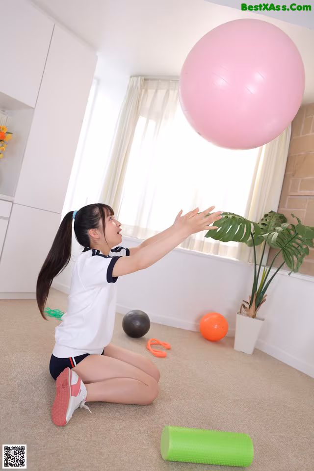 A young girl sitting on the floor playing with a pink ball.