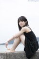 A woman in a black dress sitting on a concrete wall.