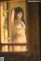 A naked asian woman standing in front of a window.