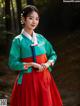 A woman in a red and green hanbok poses for a picture.