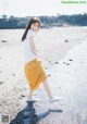 A woman in a white shirt and yellow skirt walking on a beach.