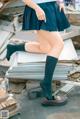 A woman in a school uniform is sitting on a pile of books.