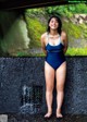 A woman in a blue bathing suit standing next to a waterfall.