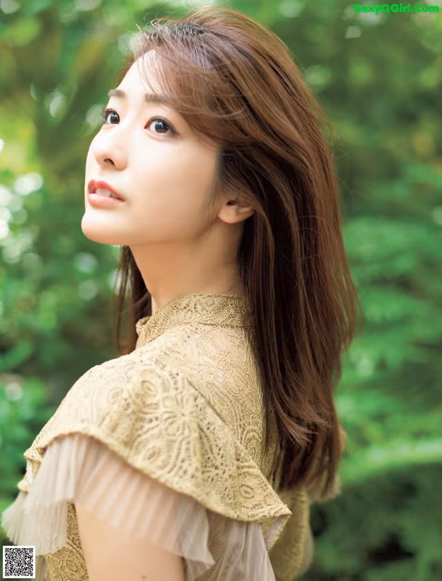 A woman with long brown hair wearing a beige dress.